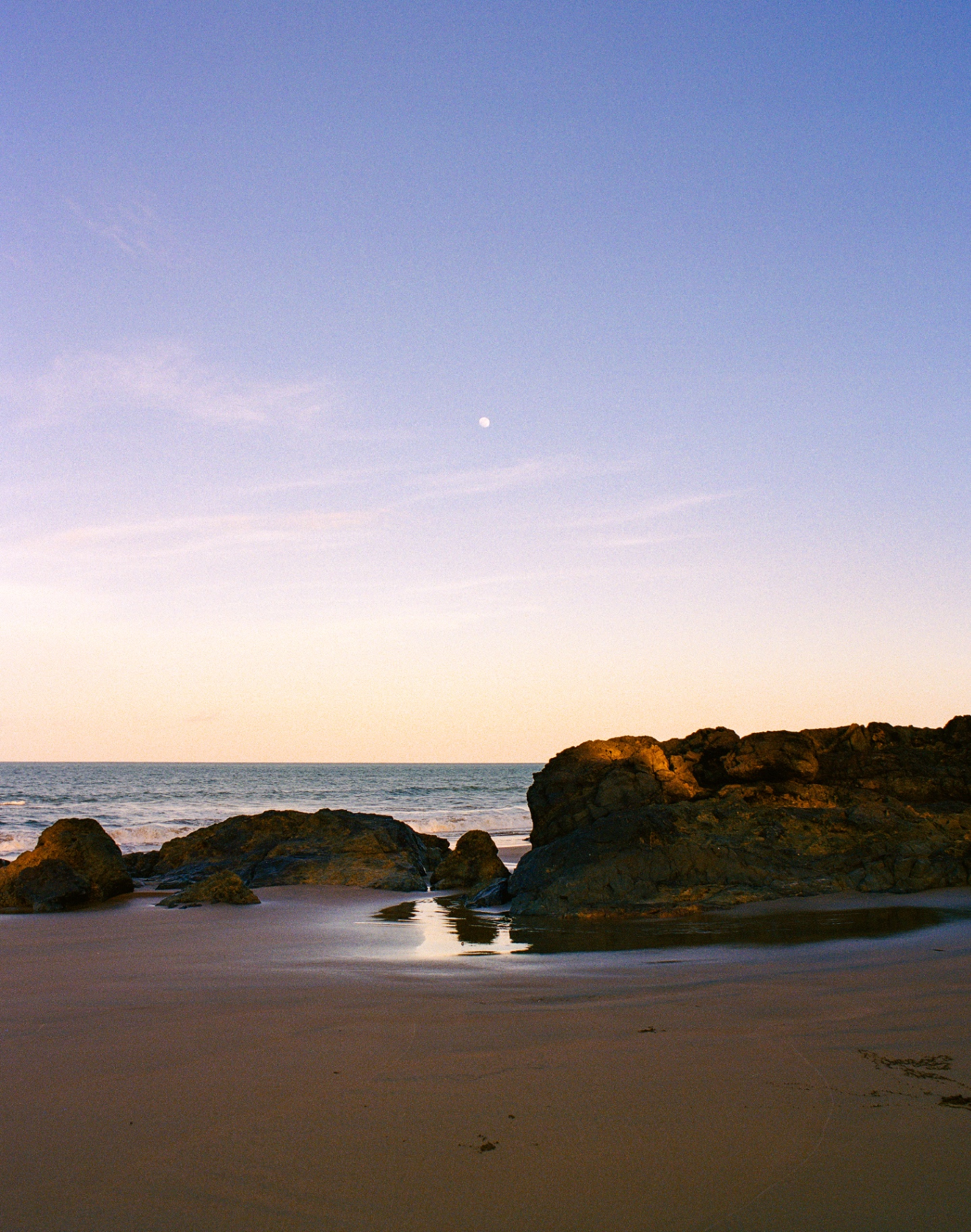 Felsen am Strand bei Abenddämmerung mit Mond über dem Meer